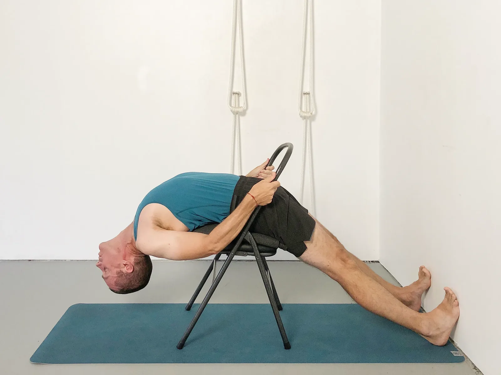 Rod arched back over a chair, holding the chair, with his feet against the wall.